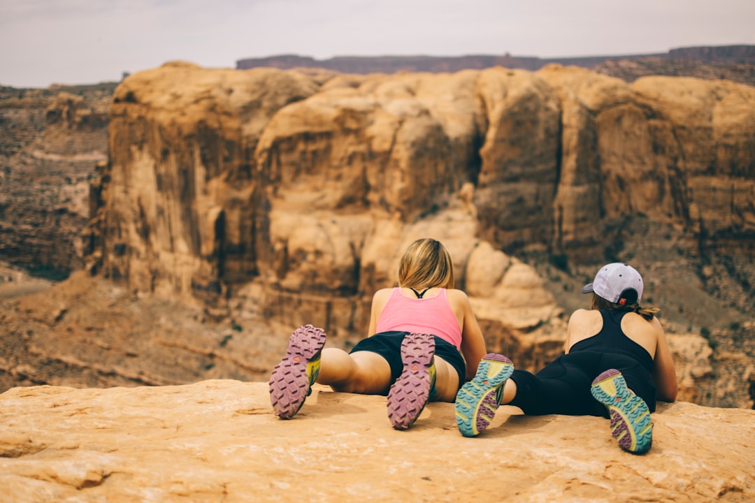 two woman lying face down on top of rock cliff overlooking cliff at daytime