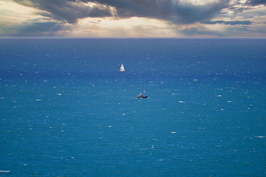 a sailboat in the middle of the ocean under a cloudy sky